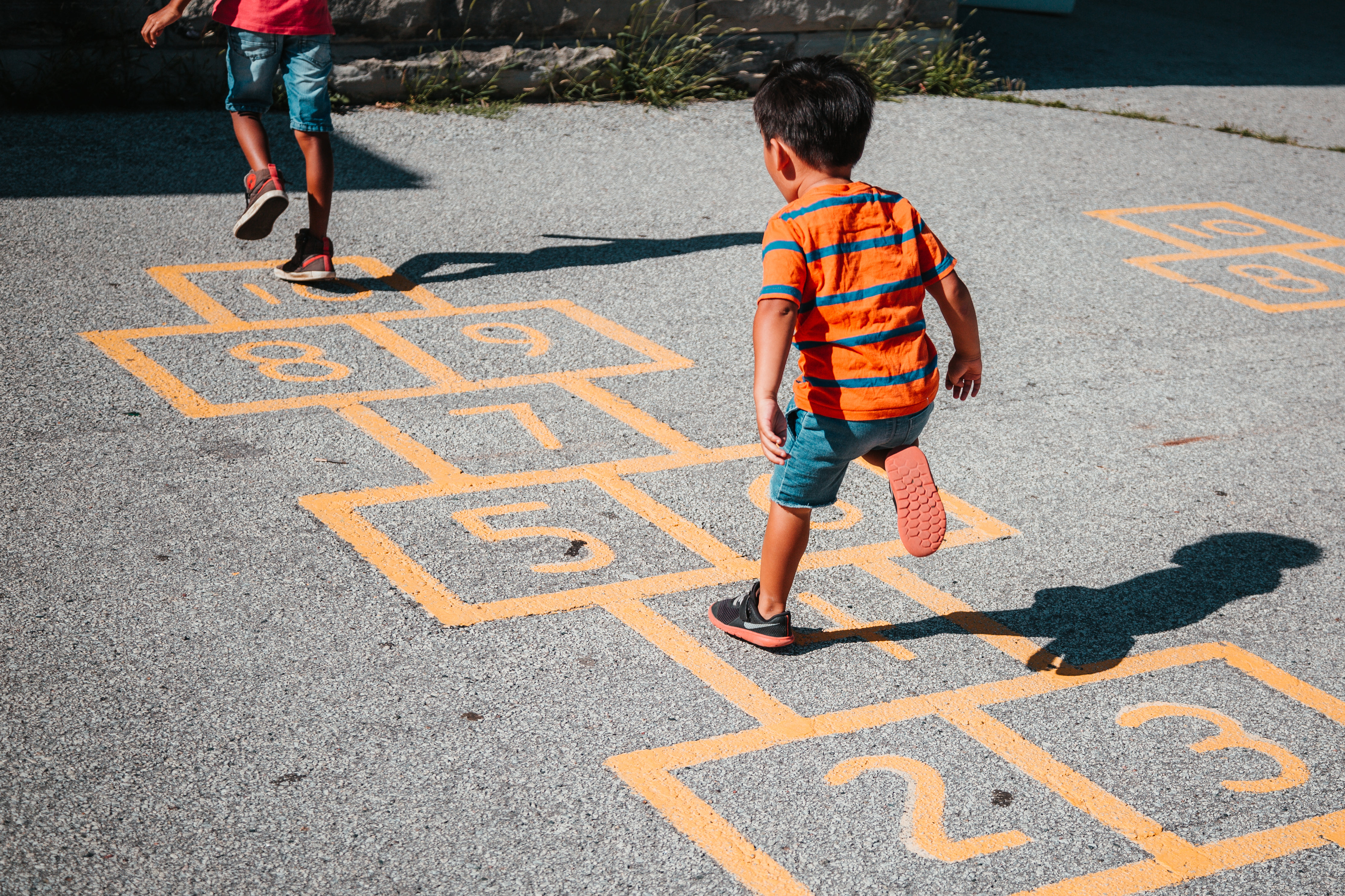 A toddler in an orange striped shirt playing hopscotch.